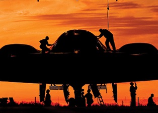 Photo of 131st Bomb Wing Maintainers working on and around a B-2 Spirit stealth bomber at sunset.